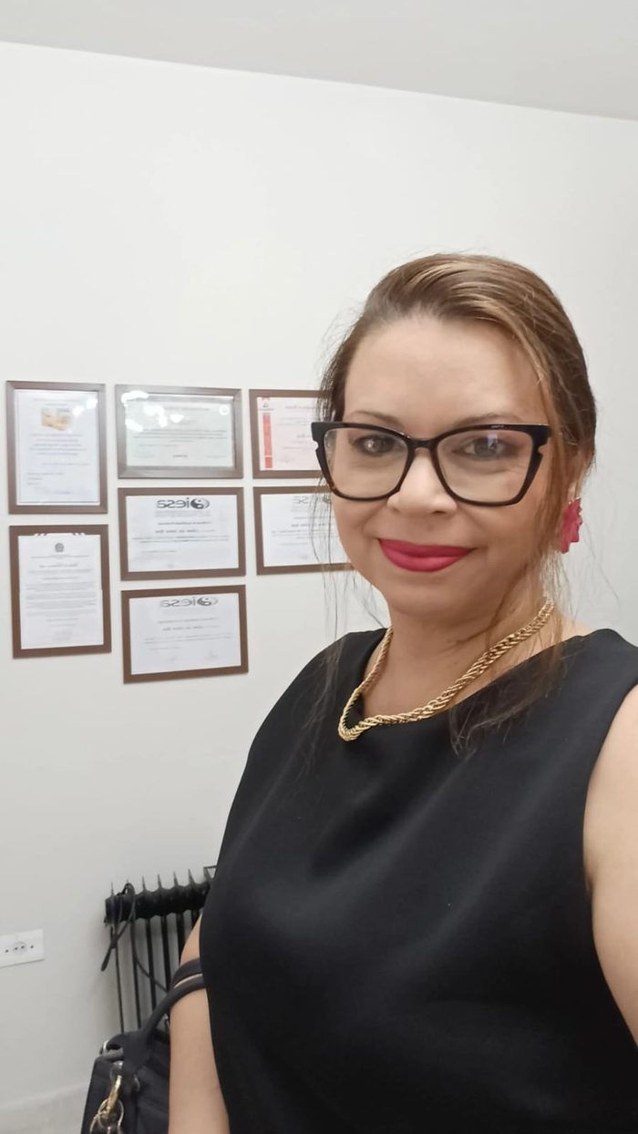 Dra. Liliana Rosa em seu consultório, com certificações e formações ao fundo